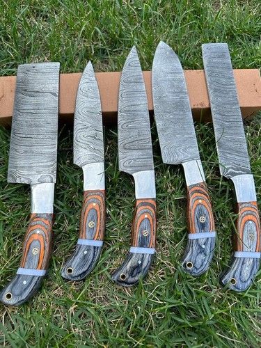 Complete 5 piece custom Damascus kitchen knife set with wooden handles on rustic wood background.